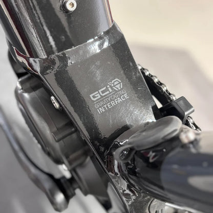 Izdelek je električno kolo, znamke Raymon, model GravelRay E 7.0. Na sliki je vidna spodnja opora kolesa, kjer je označen sistem "Gravity Casting Interface". Vidni so tudi detajli, kot so del motorja in povezava s verigo, kar nakazuje na robustno konstrukcijo kolesa.