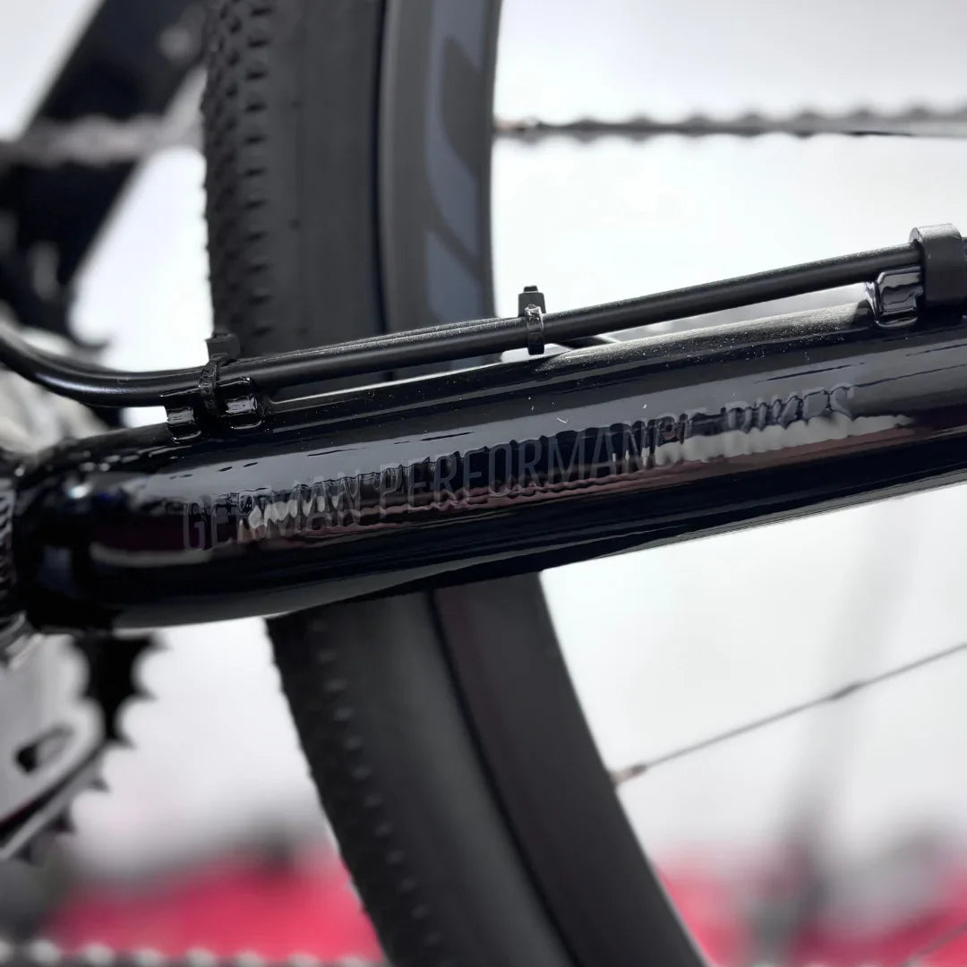 Izdelek je električno kolo, znamke Raymon, model GravelRay E 7.0. Na sliki je del okvirja kolesa, ki je črne barve, z vidnimi detajli, kot so kabli in zobniki. Oprema kaže na kakovostno izdelavo, kar je značilno za to znamko. Kolo je namenjeno vožnji po gravel površinah in nudi dobro zmogljivost.