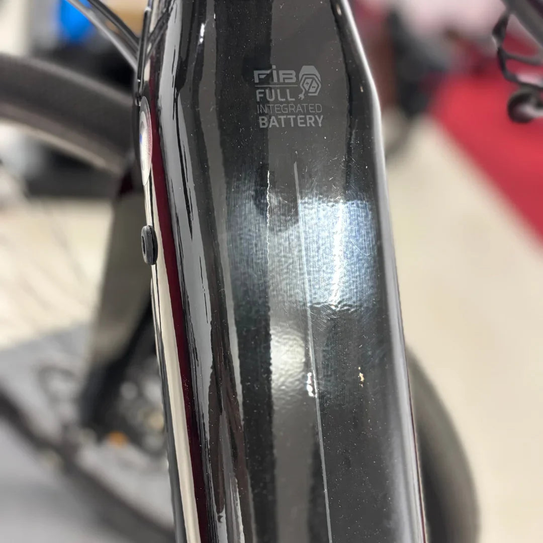 Na sliki je električno kolo znamke Raymon, model GravelRay E 7.0. Vidna je baterija, ki je popolnoma integrirana v okvir kolesa, kar daje kolesu eleganten videz. Kolo ima črno barvo in sodoben dizajn, kar je značilno za tovrstne električne modele.