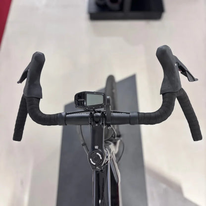 Izdelek je električno kolo, znamke Raymon, model GravelRay E 7.0. Na sliki je vidna sprednja stran krmila, ki ima športne ročke in digitalni zaslon, verjetno za prikaz informacij o vožnji. Kolo ima tudi elegantno črno barvo in je zasnovano za gravel vožnjo.