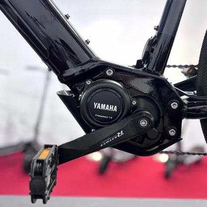 Izdelek na sliki je električno kolo, model Raymon GravelRay E 7.0. Na sliki je prikazan motor Yamaha, ki je nameščen na okvirju kolesa, kar kaže na njegovo zmogljivost in tehnologijo. Vidna je tudi pedalna enota, kar nakazuje na funkcionalnost in zasnovo kolesa.