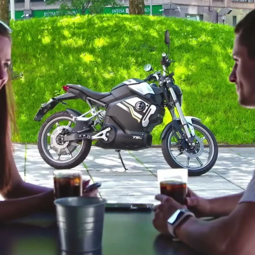 Par uživa v pijači v kavarni, v bližini pa je parkiran električni skuter Super Soco Tsx.