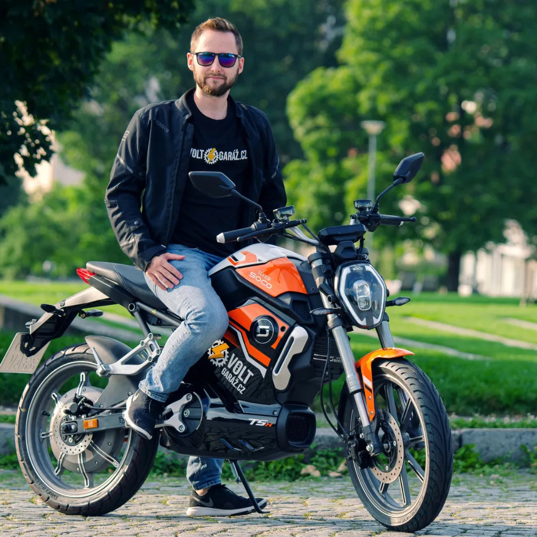 Moški sedi na električnem skuterju Super Soco Tsx v parku.