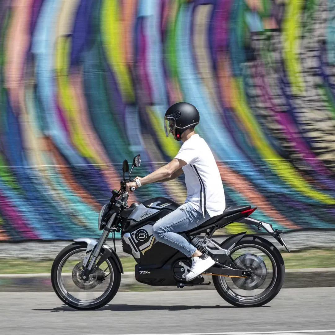 Voznik električnega skuterja Super Soco Tsx pred pisanim grafitnim ozadjem.