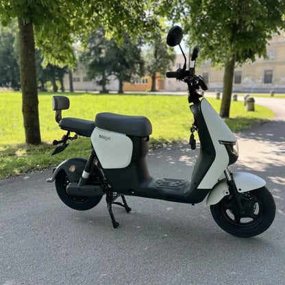 Na sliki je električni skuter, znamke Saigo. Izdelek ima moderno obliko, z udobnim sedežem in širokimi pnevmatikami. V ozadju je zeleno okolje, kar nakazuje na uporabo v mestnem okolju. Skuter je zasnovan za enostavno in udobno vožnjo.