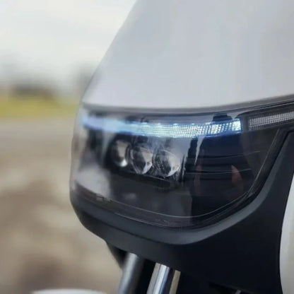 Na sliki je vidna sprednja luč električnega motocikla, ki pripada znamki Stromko. Luč ima sodoben dizajn z LED tehnologijo, kar kaže na napreden pristop k osvetlitvi. Vidni so tudi detajli, kot so reflektorji in obroba luči, ki dopolnjujejo estetski videz motocikla.