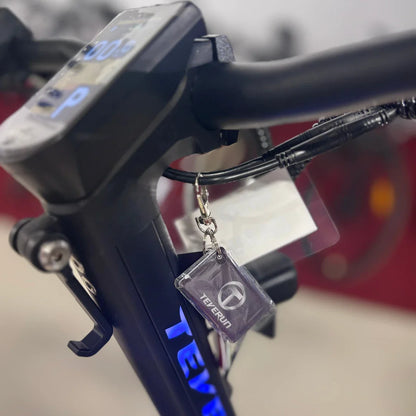 Na sliki je električni skiro, model Teverun Fighter Mini Pro 2025. Vidna je krmilo skiroja z digitalnim zaslonom, ki prikazuje podatke o vožnji, ter ključavnico s priponko znamke Teverun. Oprema je v črni barvi, kar daje skiroju sodoben videz.