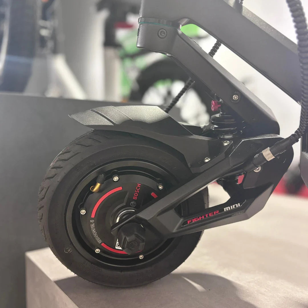 Izdelek na sliki je električni skiro, model Teverun Fighter Mini Pro 2025. Vidna je zadnja kolesna enota, ki vključuje motor Bosch ter del podvozja, ki je zasnovan za stabilnost in udobje vožnje. Kolo ima robusten profil pnevmatike, kar nakazuje na dobro oprijemljivost na različnih površinah.