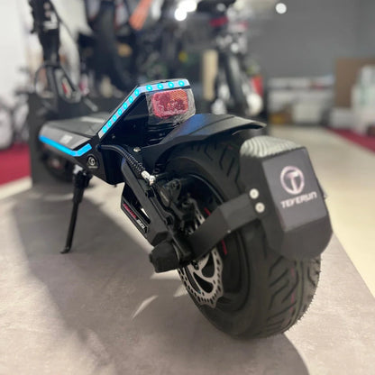 Na sliki je električni skiro, model Teverun Fighter Mini Pro 2025. Vidna je zadnja stran skiroja, ki ima LED luči in široko pnevmatiko. Na skiroju je tudi disk zavora, kar nakazuje na njegovo zmogljivost in varnost pri vožnji. Zasnova je moderna in športna, kar privlači pozornost.