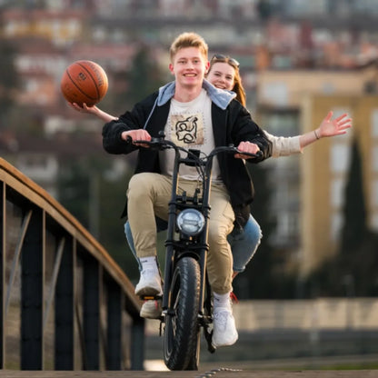 Mladenič se vozi z električnim kolesom Tomos Flexer, za njim pa dekle drži košarkarsko žogo.