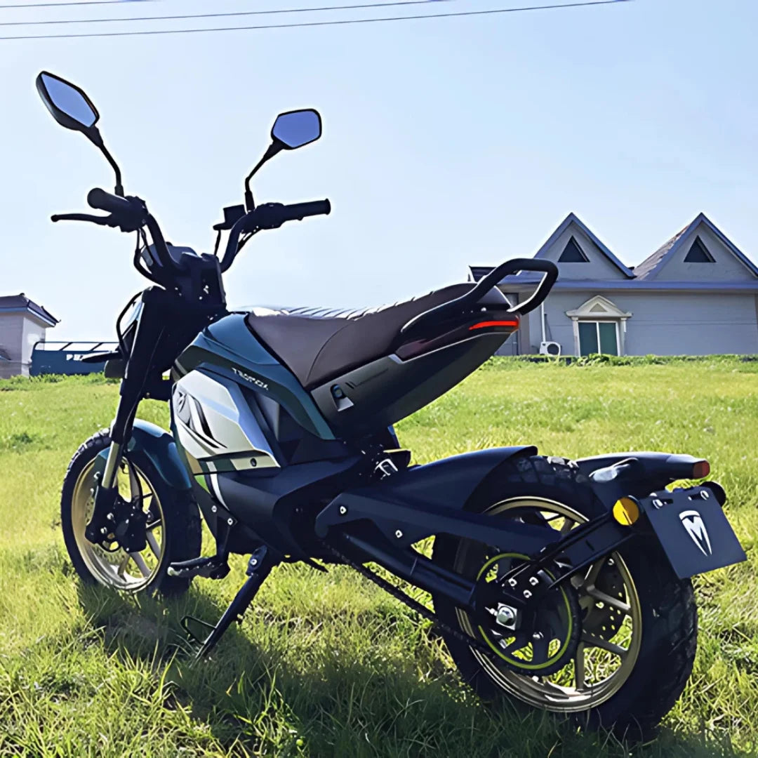 Električni skuter Tromox Mino B parkiran na travi z jasnim modrim nebom v ozadju.
