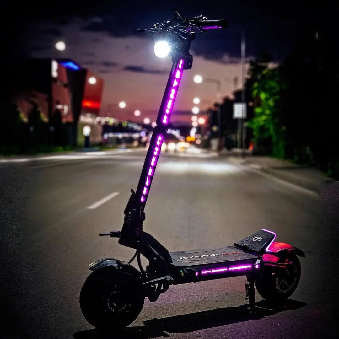 Električni skiro Teverun Fighter 11 Plus parkiran na ulici, osvetljen z živahnimi lučmi v mraku.