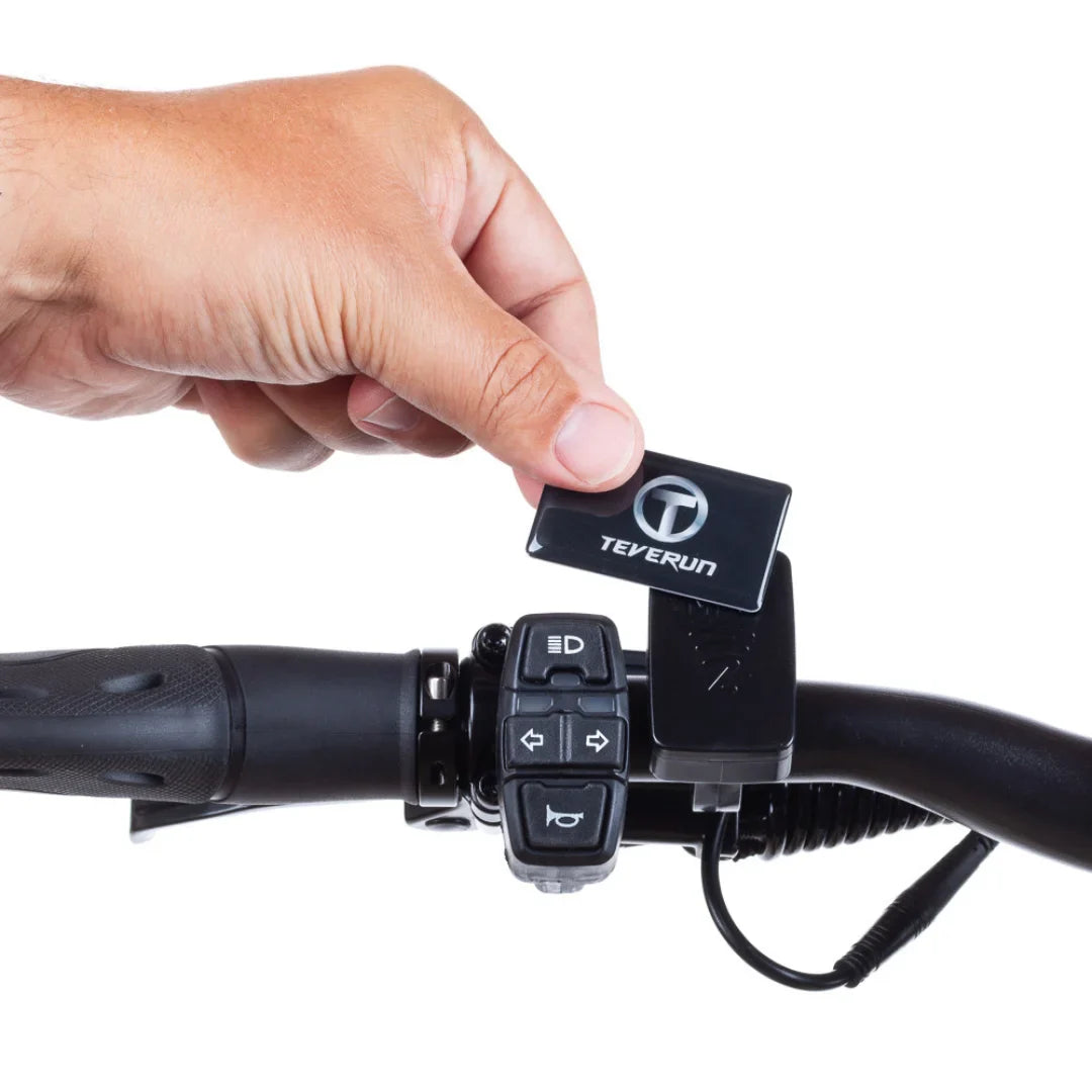 Na sliki je prikazan električni skiro znamke Teverun, model Fighter Mini Pro 2025. Vidna je roka, ki drži ključek z logotipom Teverun, medtem ko je skiro v ozadju. Na krmilu skiroja so tudi gumbi za upravljanje, kar nakazuje na funkcionalnosti vozila.