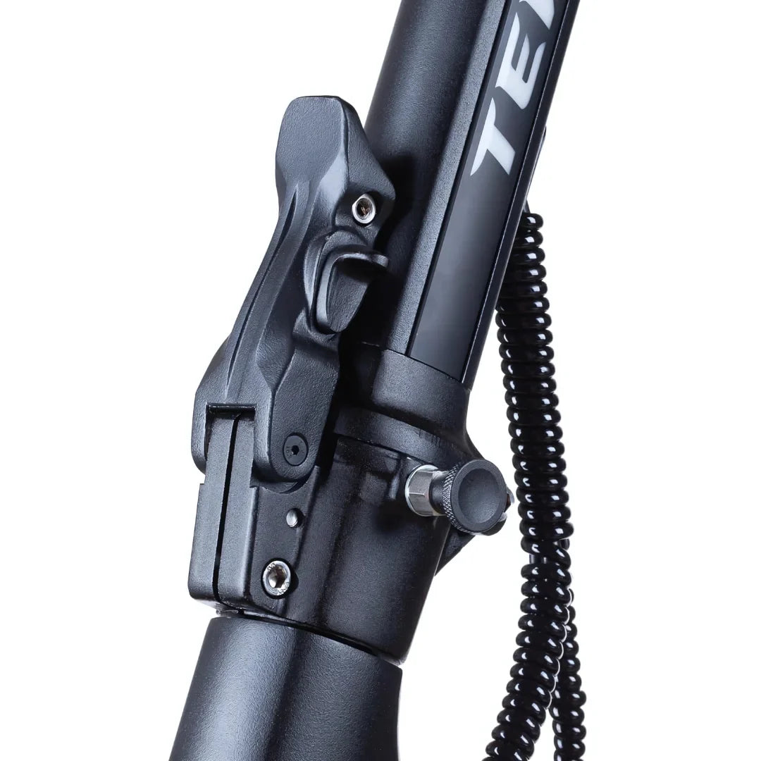 Izdelek na sliki je električni skiro, model Teverun Fighter Mini Pro iz leta 2025. Na sliki je prikazano območje, kjer se nahaja mehanizem za zlaganje skiroja, vključno z gumbom in nekaterimi detajli okvirja. Barva je temna, kar daje izdelku sodoben in robusten videz.