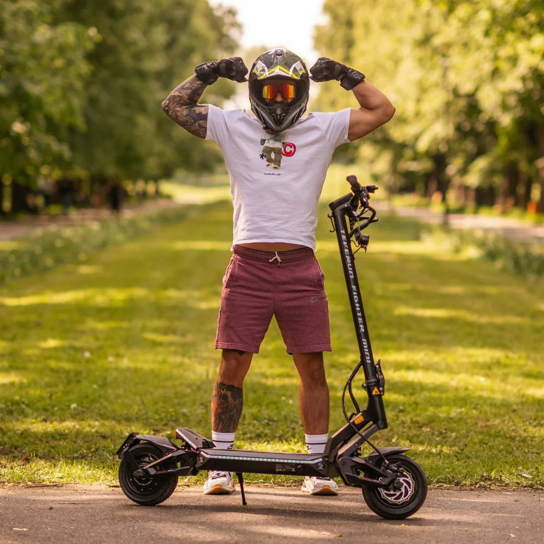 Oseba s čelado napenja mišice na električnem skiroju Teverun Fighter Mini v parku.