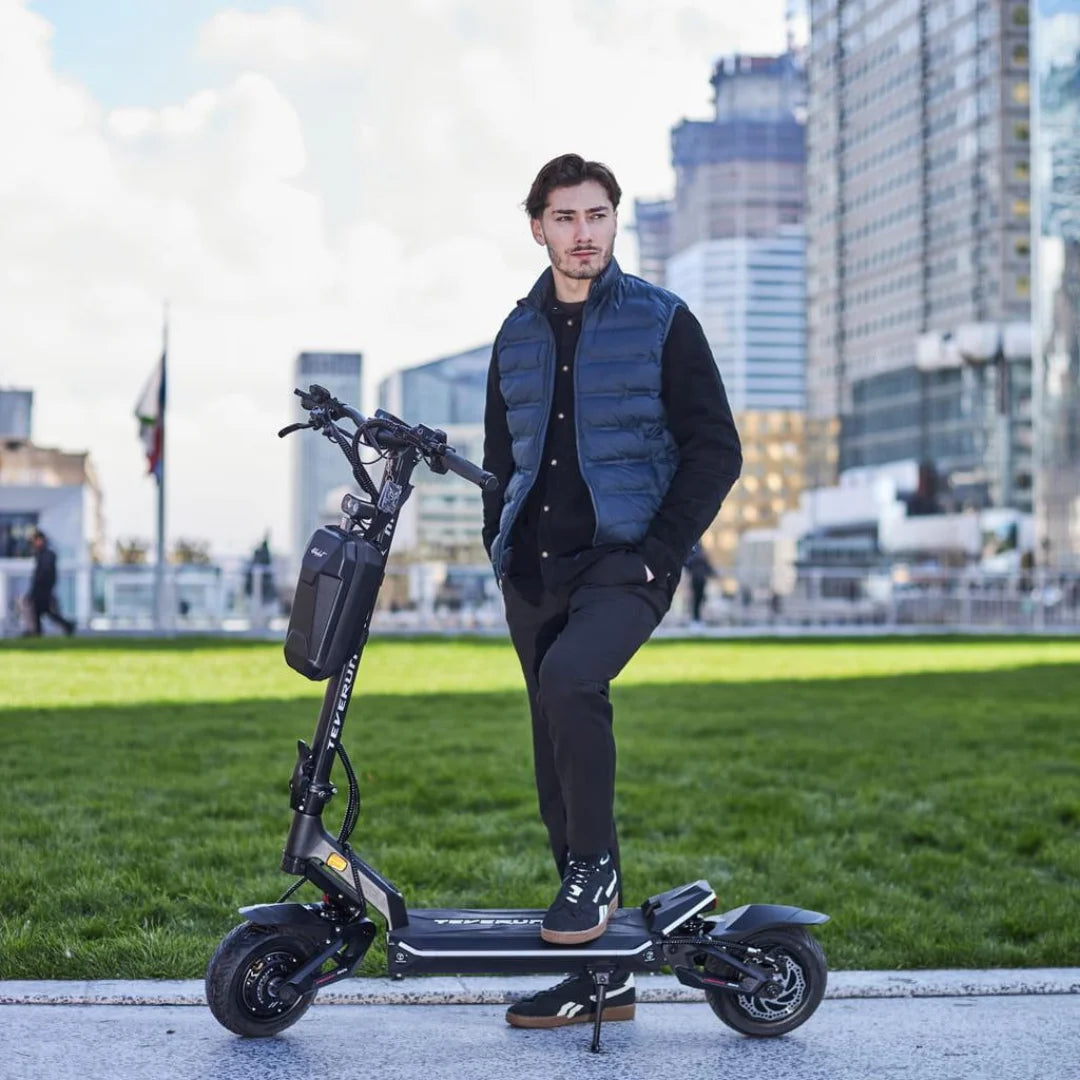 Moški stoji na električnem skiroju Teverun Fighter Mini v urbanem parku.