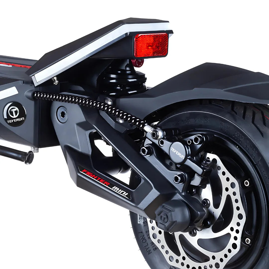 Izdelek je električni skiro, model Teverun Fighter Mini Pro 2025. Na sliki je prikazan zadnji del skiroja, kjer so vidni amortizer, disk zavorni sistem in kolesa. Zasnova je moderna, s poudarjenimi linijami in robustno konstrukcijo, kar nakazuje na visoko kakovost in zmogljivost. Osvetljava na zadnjem delu je prav tako jasno vidna, kar povečuje varnost pri vožnji.