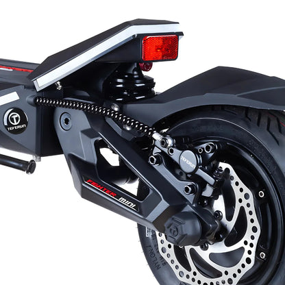 Izdelek je električni skiro, model Teverun Fighter Mini Pro 2025. Na sliki je prikazan zadnji del skiroja, kjer so vidni amortizer, disk zavorni sistem in kolesa. Zasnova je moderna, s poudarjenimi linijami in robustno konstrukcijo, kar nakazuje na visoko kakovost in zmogljivost. Osvetljava na zadnjem delu je prav tako jasno vidna, kar povečuje varnost pri vožnji.