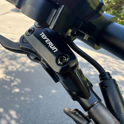 Izdelek je električni skiro, znamke Teverun, model Fighter Mini Pro 2025. Na sliki je prikazan del krmila skiroja, kjer je vidna ročica za zaviranje in del mehanizma, ki vključuje oznako znamke Teverun. Oprema izgleda robustno in sodobno, kar nakazuje na kakovost in zmogljivost izdelka.