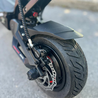 Izdelek na sliki je električni skiro, model Teverun Fighter Mini Pro 2025. Vidna je zadnja kolesna enota, ki vključuje disk zavore in pnevmatik z izrazitim profilom, kar nakazuje na dobro oprijemljivost. Na sliki je tudi del okvirja skiroja, kar daje občutek robustnosti in trajnosti izdelka.