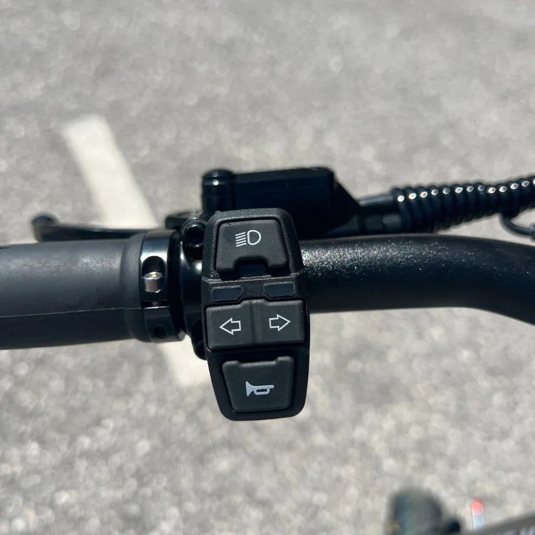 Na sliki je prikazan električni skiro, model Teverun Fighter Mini Pro 2025. Vidna je ročica na krmilu, ki vsebuje gumbe za luči, smerokaze in trobento. Ta zasnova omogoča enostavno upravljanje funkcij med vožnjo, kar povečuje varnost in udobje uporabnika.