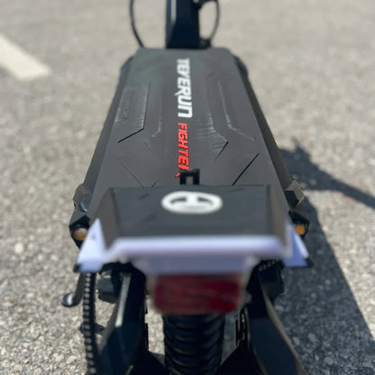 Na sliki je električni skiro znamke Teverun, model Fighter Mini Pro iz leta 2025. Vidna je platforma skiroja z oznako "Teverun Fighter" v rdeči barvi, ki je postavljena na črni površini. Na sprednjem delu skiroja je tudi svetilka, kar nakazuje na funkcionalnosti, ki so značilne za ta tip vozila.