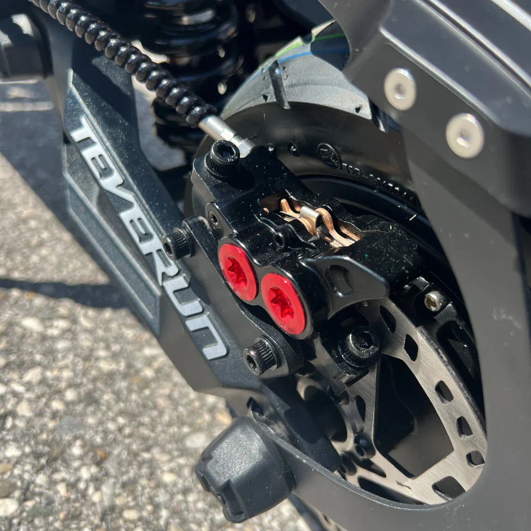 Izdelek na sliki je električni skiro, model Teverun Fighter Mini Pro 2025. Vidna je podrobnost zavornega sistema, kjer so prikazane rdeče vijake in del zavorne ploščice. Skira je zasnovan za učinkovito zaviranje in stabilnost pri vožnji.