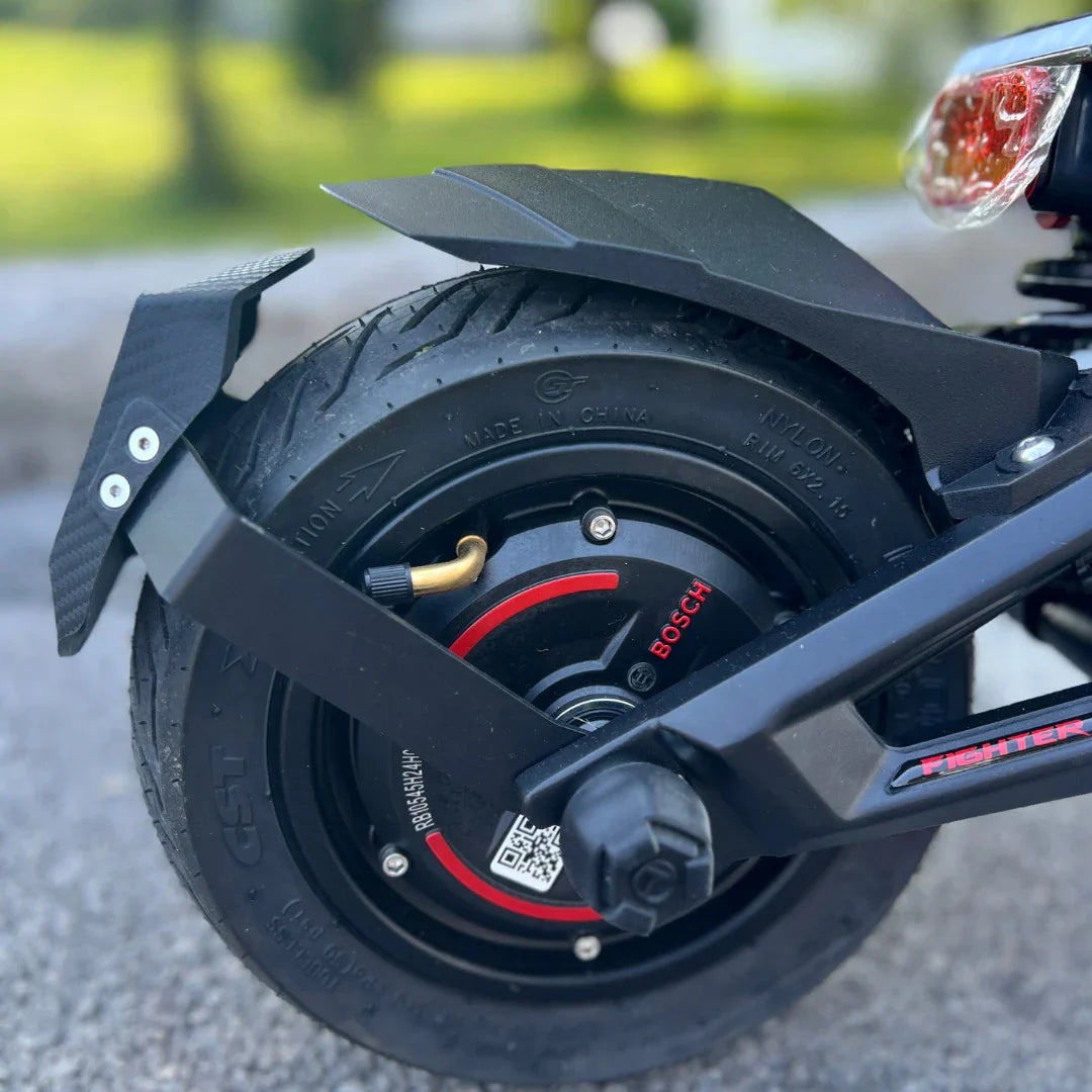 Na sliki je električni skiro, model Teverun Fighter Mini Pro iz leta 2025. Vidna je zadnja pnevmatika, ki ima robusten profil, ter motor s prikazanim imenom znamke Bosch. Na skiroju so tudi elementi za zaščito in stabilnost, kar nakazuje na njegovo zmogljivost in kakovost.