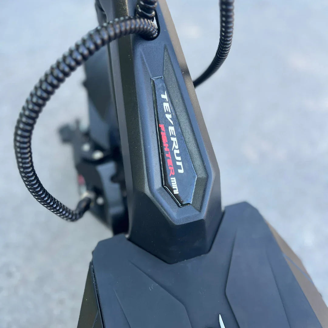 Izdelek na sliki je električni skiro znamke Teverun, model Fighter Mini. Na sliki je del konstrukcije skiroja, ki prikazuje značilno obliko in oznako znamke. Vidna je tudi tekstura površine in detajli, ki nakazujejo na robustno zasnovo skiroja.