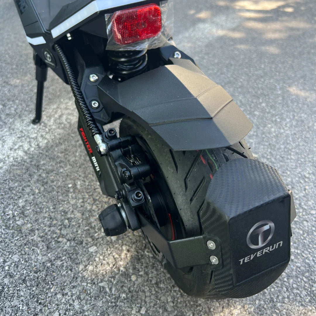 Na sliki je prikazan električni skiro, model Teverun Fighter Mini Pro 2025. Vidna je zadnja kolesna enota, ki vključuje široko pnevmatiko in zavorni sistem. Na zadnjem delu skiroja je nameščen tudi odsevnik, kar povečuje varnost pri vožnji. Zasnova skiroja je moderna in robustna, kar nakazuje na njegovo zmogljivost in stabilnost.