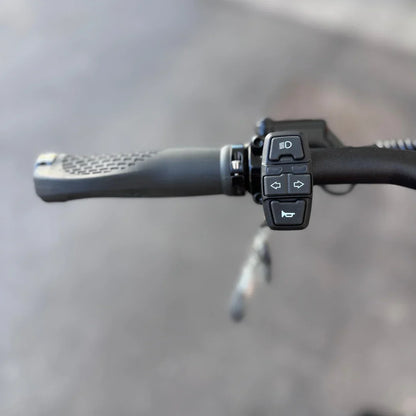 Izdelek na sliki je električni skiro, model Teverun Fighter Supreme 7260 Ultra. Na sliki je prikazan del krmila, kjer so vidne ročice in gumbi za nadzor, vključno z gumbom za luči in smerniki. Ročaji so oblikovani za udobno držanje, kar omogoča enostavno upravljanje skiroja.