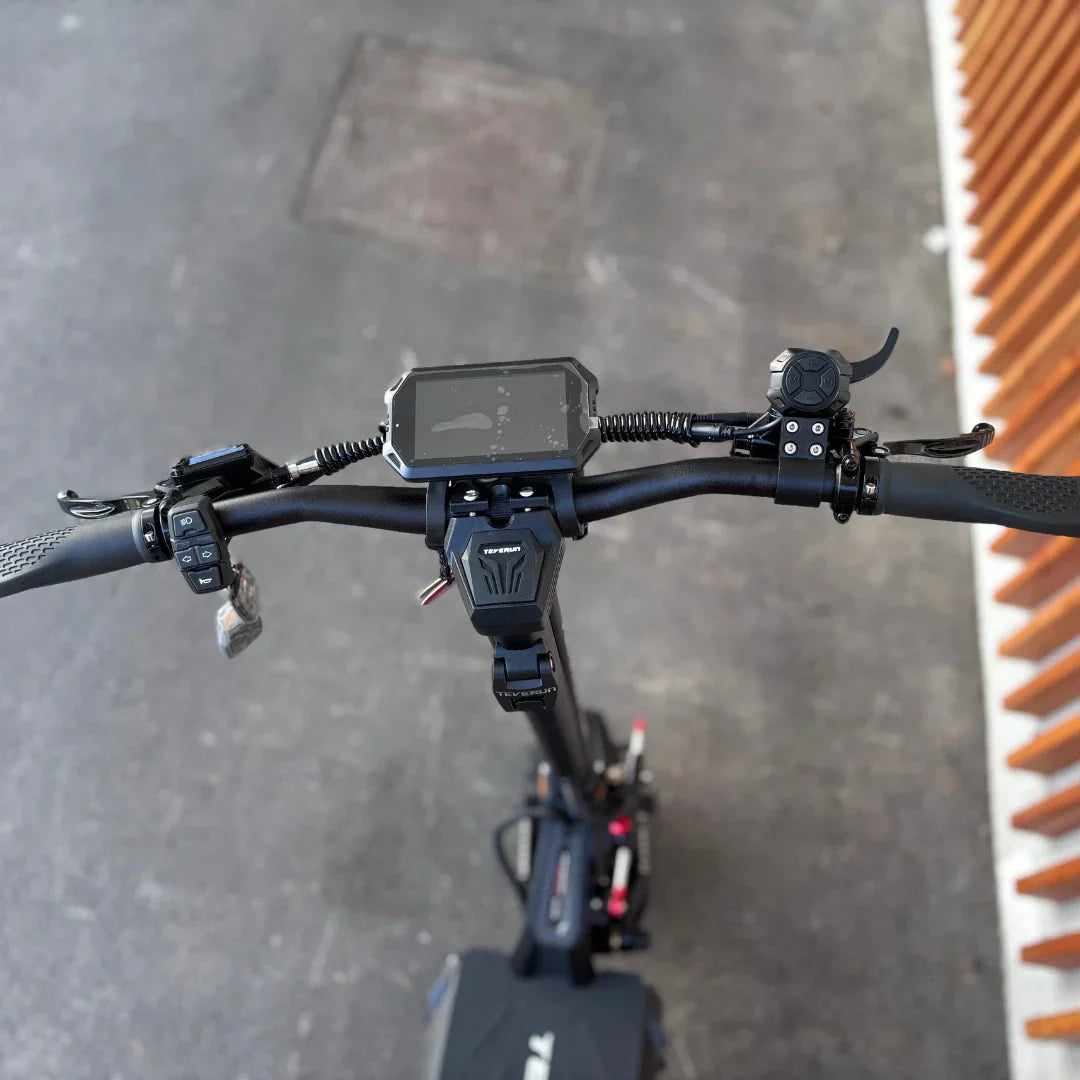 Na sliki je električni skiro, model Teverun Fighter Supreme 7260 Ultra. Vidna je nadzorna plošča z digitalnim zaslonom, ki prikazuje informacije o vožnji, ter ročaji za upravljanje. Na krmilu so tudi različni gumbi in stikala, kar omogoča enostavno upravljanje skiroja. Celoten dizajn je športen in robusten, kar nakazuje na zmogljivost in stabilnost med vožnjo.