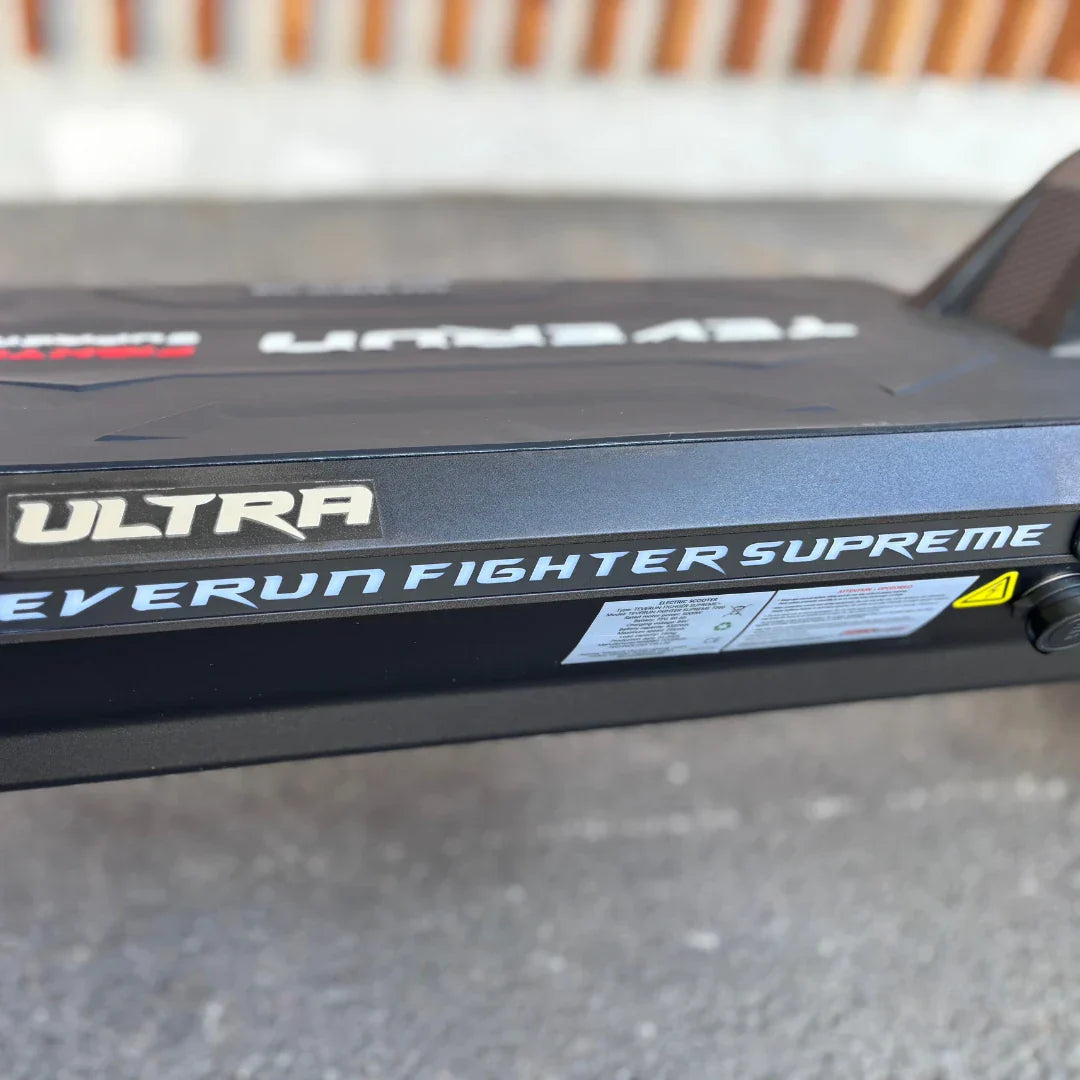 Na sliki je električni skiro znamke Teverun, model Fighter Supreme. Vidna je stranska površina skiroja, kjer je jasno označen model z napisom "Teverun Fighter Supreme" in "ULTRA". Površina skiroja je temna, z modernim in športnim dizajnom, kar nakazuje na njegovo zmogljivost in kakovost.