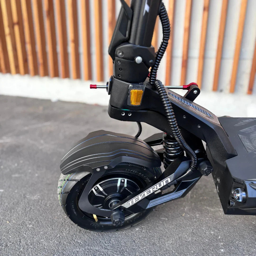 Izdelek je električni skiro, znamke Teverun, model Fighter Supreme 7260 Ultra. Na sliki je vidna sprednja kolesna enota skiroja, ki vključuje robustno kolo z značilnim vzorcem, sistem vzmetenja ter del okvirja. Kolo je opremljeno z disk zavornim sistemom, kar nakazuje na visoko zmogljivost in stabilnost pri vožnji. V ozadju je vidna lesena stena, kar daje sliki estetski pridih.