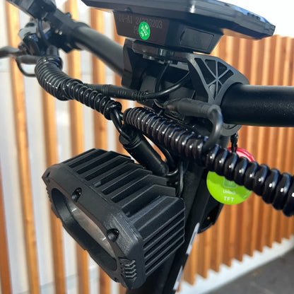 Izdelek je električni skiro, model Teverun Fighter Supreme 7260 Ultra. Na sliki je prikazan del krmila, kjer so vidni kabli, ki so organizirani v spirali, ter svetilka z robustnim ohišjem. V ozadju so vidne lesene letvice, kar daje sliki estetski videz.