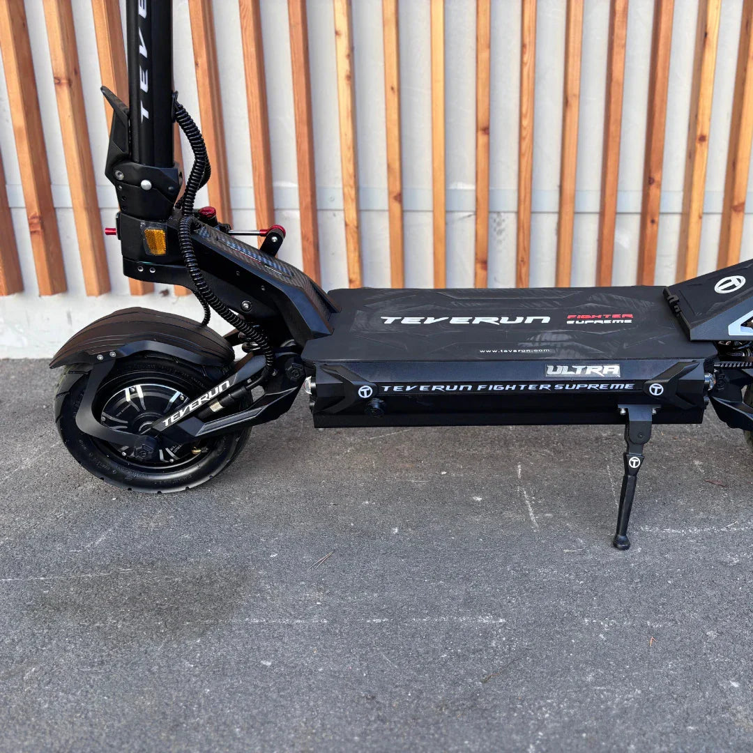 Izdelek na sliki je električni skiro, model Teverun Fighter Supreme 7260 Ultra. Vidna je robustna konstrukcija skiroja, ki vključuje široko platformo za stojišče, velike kolesa in vzmetenje. Na sprednjem delu se nahajajo luči, kar nakazuje na možnost vožnje v slabših svetlobnih pogojih. Celoten dizajn je športen in modern, kar je značilno za to znamko.