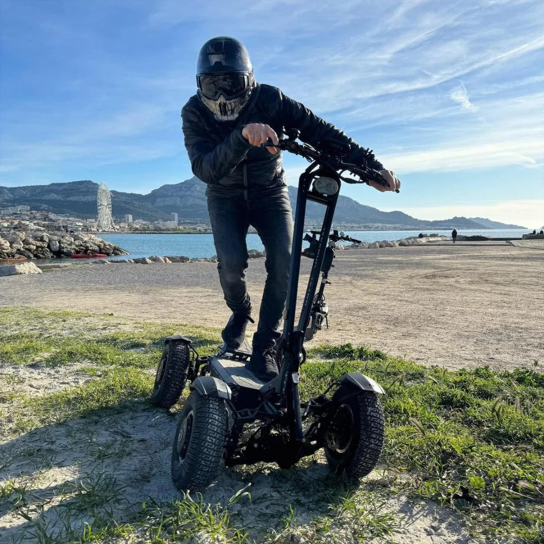 Voznik električnega skiroja Teverun Tetra 4x4 na slikoviti lokaciji ob plaži.