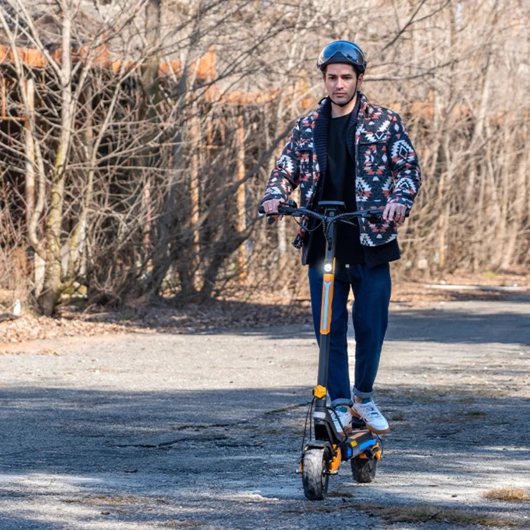 Oseba se vozi z električnim skirojem Urbanride 1000gt po makadamski poti, obdani z drevesi.