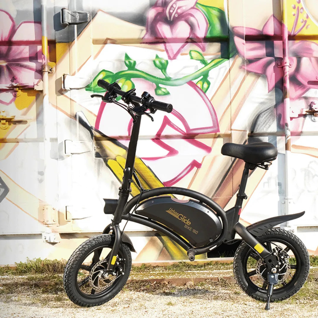 Električno kolo Urbanglide 160 parkirano ob pisani steni z grafiti.