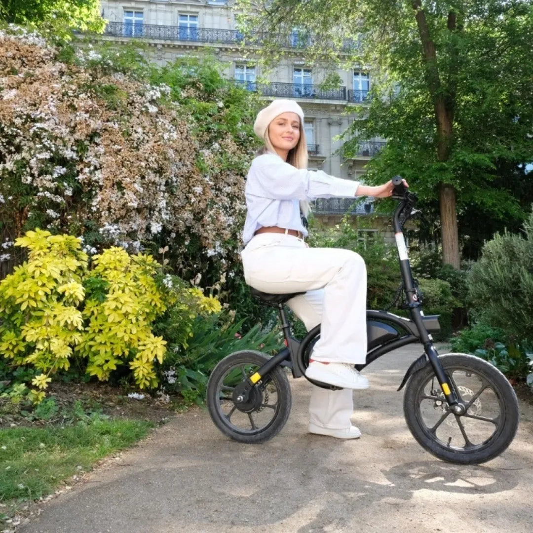 Ženska pozira na električnem kolesu Urbanglide 160 v bujnem vrtnem okolju.