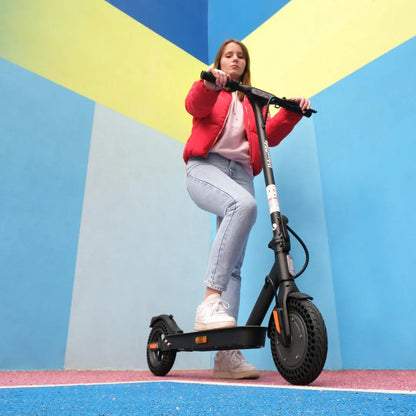 Oseba se vozi z električnim skirojem Urbanride 100xs pred pisano steno.