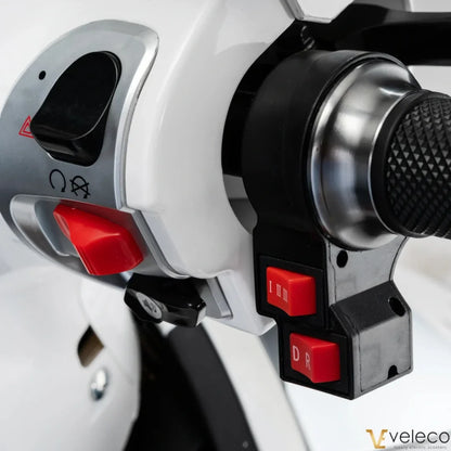 Izdelek na sliki je električni skuter, model Veleco Cristal. Vidna je upravljalna enota, ki vključuje različne gumbe za nadzor hitrosti in smeri vožnje. Na skuterju so označeni gumbi za izbiro hitrosti ter stikalo za napajanje, kar omogoča enostavno upravljanje med vožnjo.