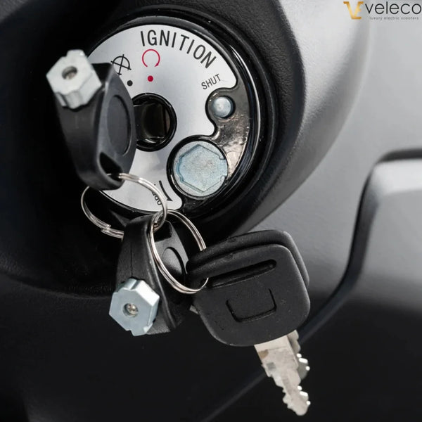 Izdelek je električni skuter, znamke Veleco, model Cristal. Na sliki je prikazan ključavnica za vžig, ki vključuje ključe in oznake za delovanje, kot so 