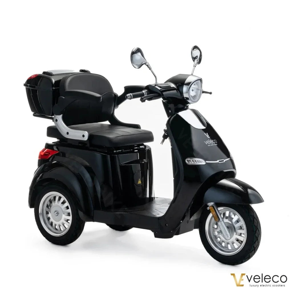 Izdelek na sliki je električni skuter, znamke Veleco, model Cristal. Skuter ima eleganten črn dizajn, udobno sedežno površino in je opremljen s sprednjimi in zadnjimi ogledali ter prostorom za shranjevanje na zadnjem delu. Ima tri kolesa, kar zagotavlja stabilnost in enostavno upravljanje.