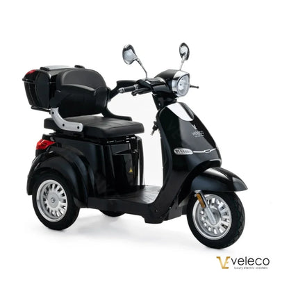 Izdelek na sliki je električni skuter, znamke Veleco, model Cristal. Skuter ima eleganten črn dizajn, udobno sedežno površino in je opremljen s sprednjimi in zadnjimi ogledali ter prostorom za shranjevanje na zadnjem delu. Ima tri kolesa, kar zagotavlja stabilnost in enostavno upravljanje.