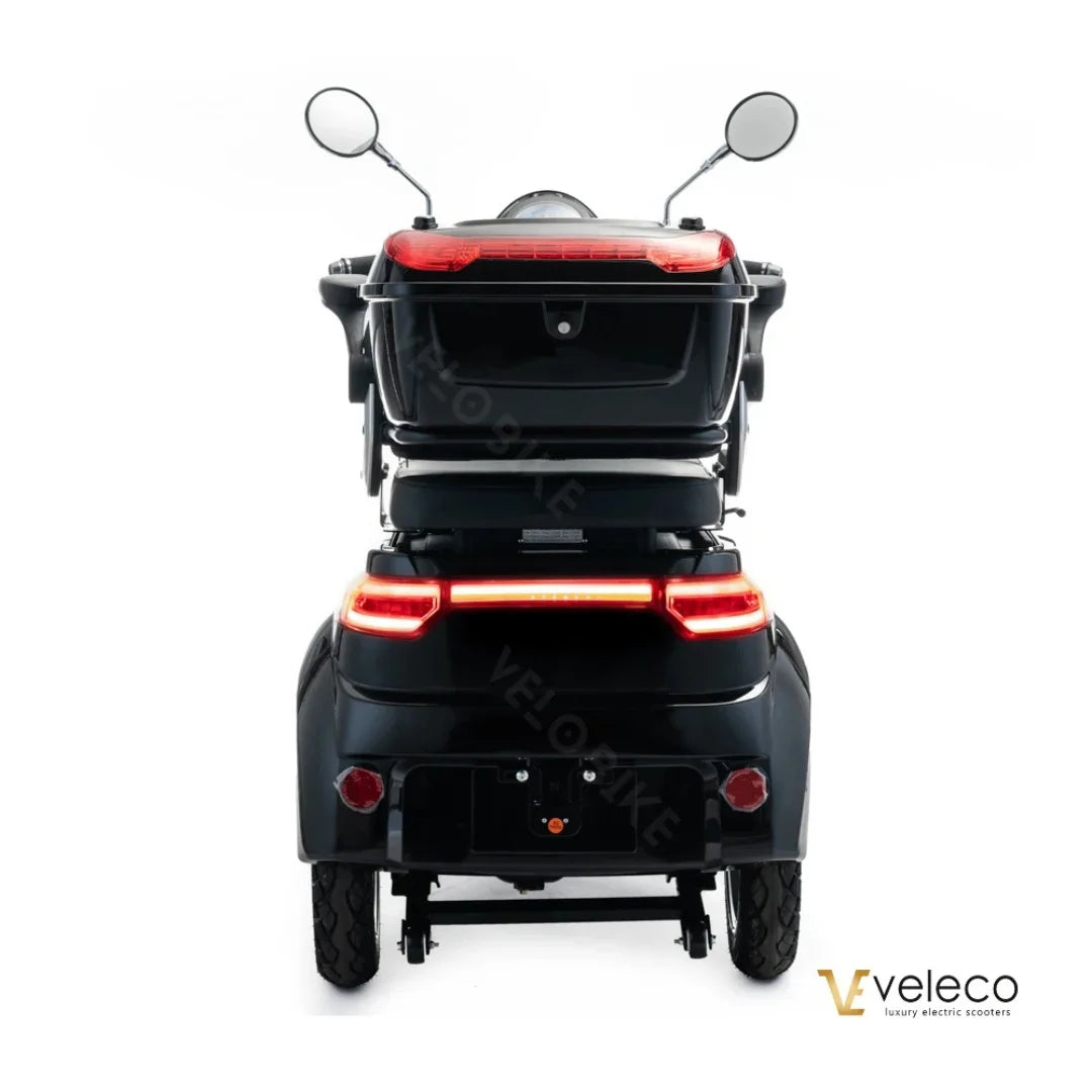 Na sliki je električni skuter, model Veleco Cristal. Izdelek ima tri kolesa, kar omogoča stabilno vožnjo, ter je opremljen z ogledali in zadnjimi lučmi. Skuter je črne barve in ima prostor za shranjevanje, kar povečuje njegovo funkcionalnost.