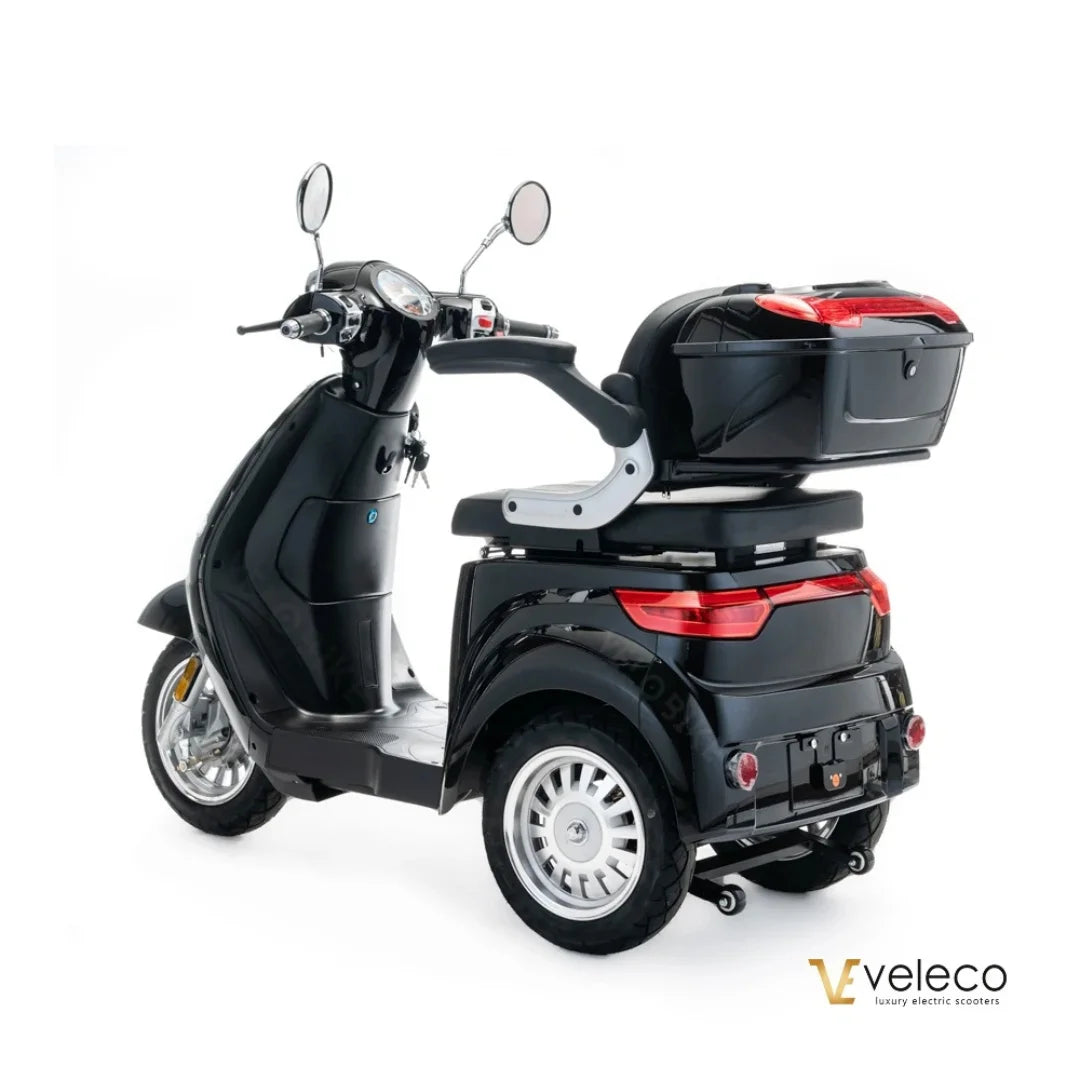 Izdelek je električni skuter, znamke Veleco, model Cristal. Na sliki je prikazan črn skuter s tremi kolesi, ki ima udoben sedež in prtljažnik na zadnjem delu. Vidni so tudi ogledali ter merilniki na krmilu, kar nakazuje na funkcionalnost in udobje med vožnjo.