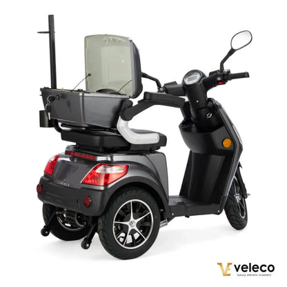 Izdelek na sliki je električni skuter, model Veleco Draco. Na sliki je vidna zasnova skuterja, ki ima tri kolesa, kar zagotavlja stabilnost. Na zadnjem delu je nameščen prostor za shranjevanje, ki je odprt, in ima udobno sedežno mesto. Skuter je v temno sivi barvi in ima sodoben izgled, kar ga naredi privlačnega za uporabnike.