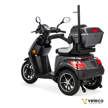 Izdelek na sliki je električni skuter, model Veleco Draco. Na sliki je vidna zadnja stran skuterja, ki ima tri kolesa, kar zagotavlja stabilnost. Skuter je opremljen s prostornim prtljažnikom na zadnjem delu ter ima udobno sedežno mesto. Vidni so tudi ogledali in merilnik na krmilu, kar nakazuje na funkcionalnost in udobje pri vožnji.