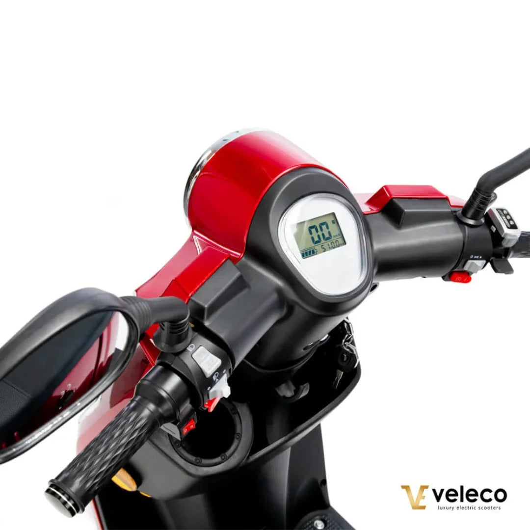 Izdelek je električni skuter znamke Veleco, model Draco. Na sliki je prikazan del krmila, ki vključuje digitalni zaslon s prikazom hitrosti in prevožene razdalje. Vidni so tudi ročaji za upravljanje ter ogledalo, kar nakazuje na funkcionalnost in udobje pri vožnji. Skuter ima sodoben in eleganten dizajn, prevladuje rdeča barva.